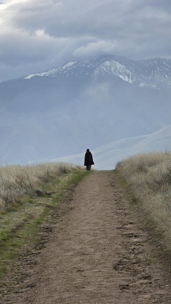 a-single-figure-walking-forward-on-a-long-unpaved-path-viewed-from-behind