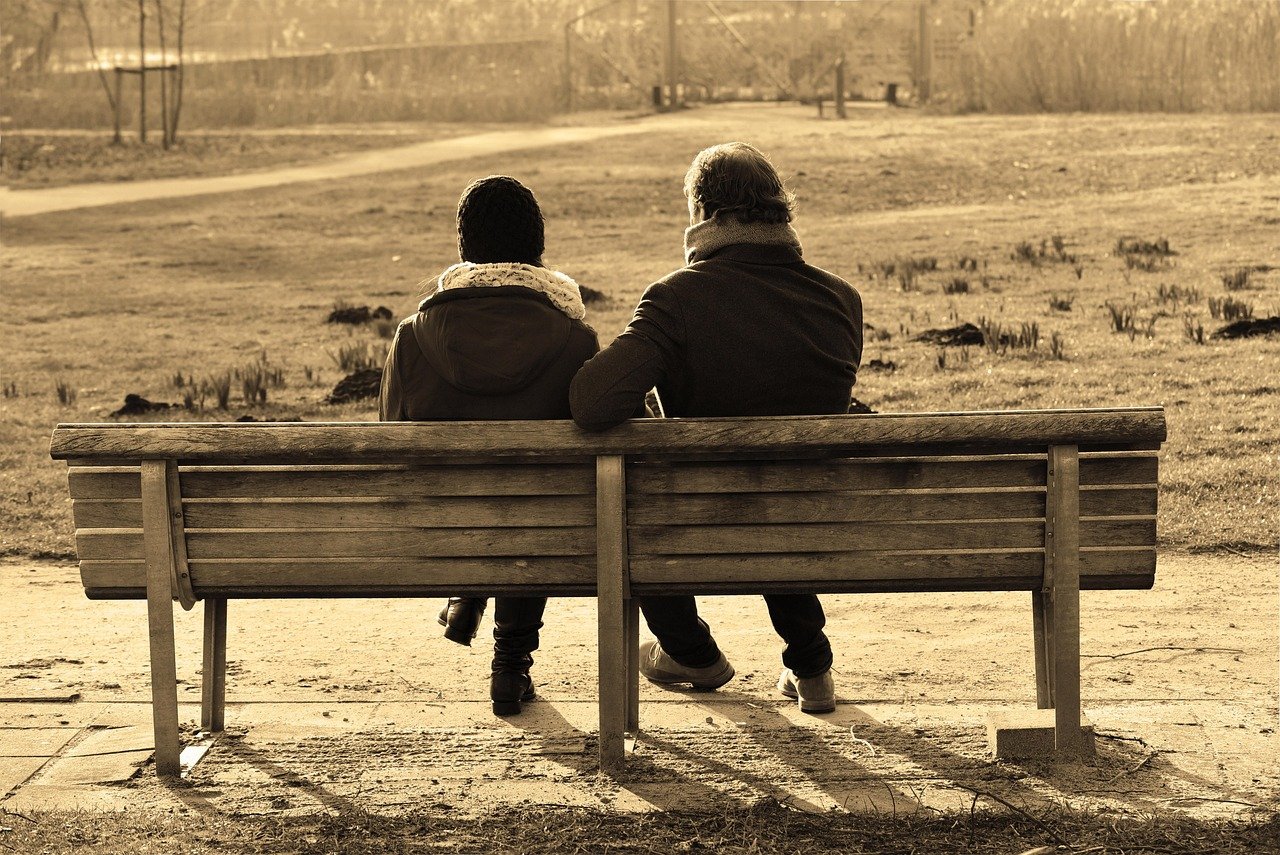 Two-people-sitting-together-on-a-bench-or-step-in-low-evening-light