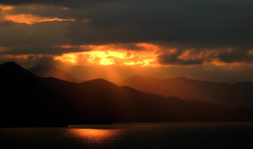 small-rocky-island-in-a-dark-open-sea-at-dusk-one-light-burning-on-it